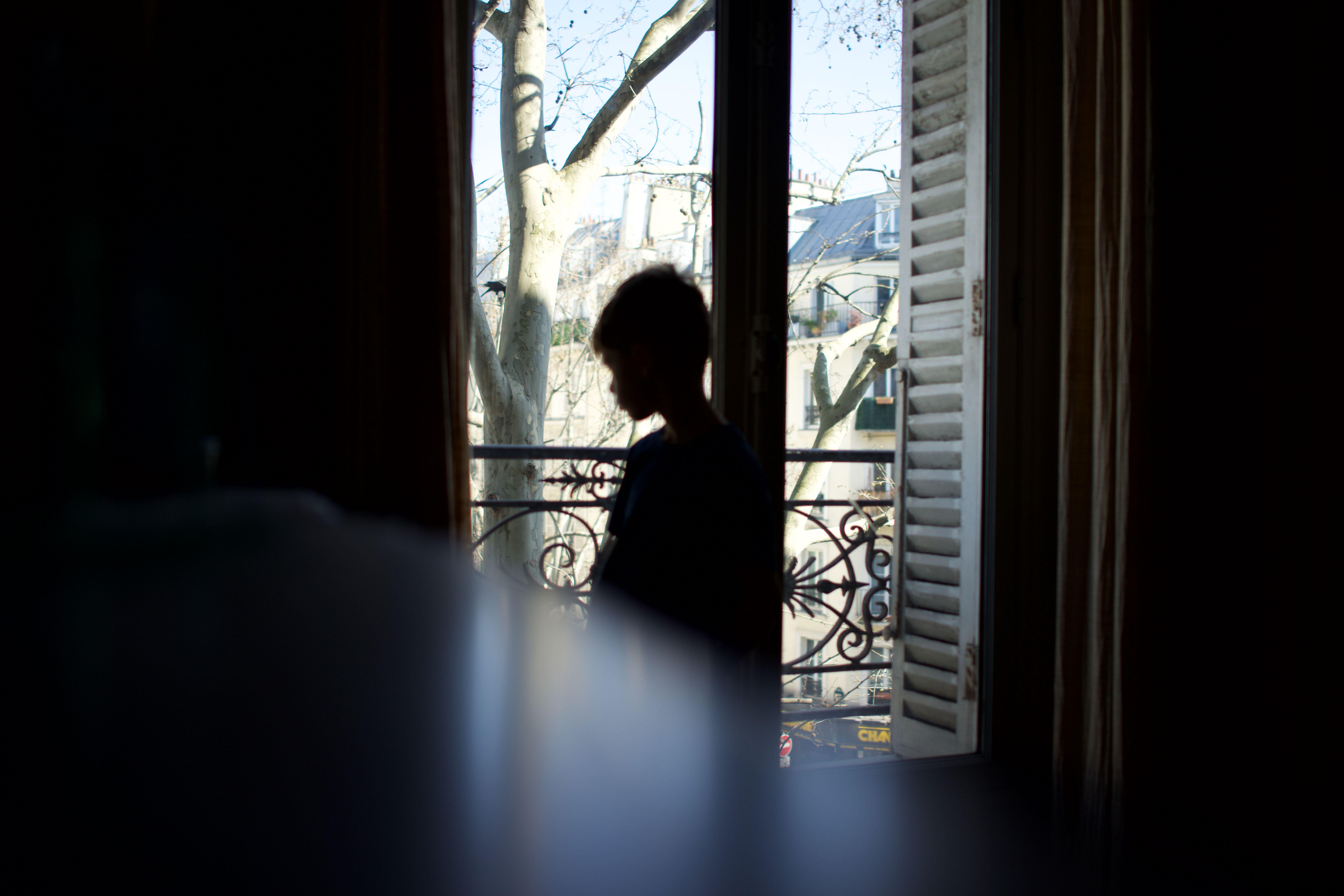 Child standing, silhouetted, looking out of window, in profile, vulnerable, alone - April 2021 confinement, Paris, France